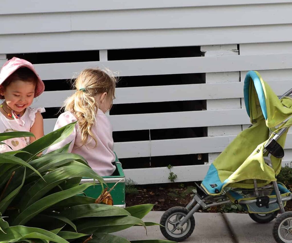 Girls playing outdoors, with baby buggy and cart at a NZ preschool